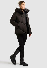 Giacca a vento nera con ampio cappuccio e quilting a rombi. Indossata sopra un outfit nero, abbinata a stivali neri con suola chunky al ginocchio.