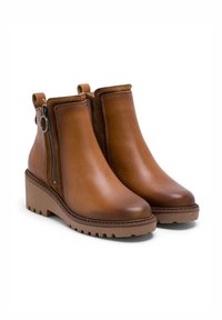 Botas de tobillo de cuero marrón con tacón ancho, cremallera lateral, punta redondeada y suela texturizada. Acabado suave con un detalle de costura mínima.