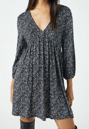 Robe à imprimé floral noir avec un col en V, des manches longues et des fronces au niveau de la poitrine. Confectionnée en tissu léger, longueur genoux avec une coupe ample.