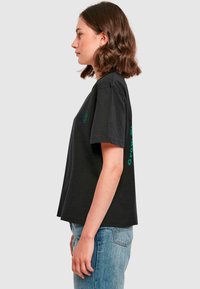 Sort bomulds t-shirt med afslappet pasform, korte ærmer og grøn grafisk tekstdesign på siden. Glat tekstur og crew neck.