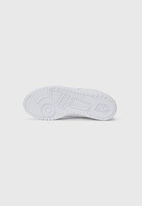 Hvit sneaker såle med Puma-logo, teksturerte grep mønstre, samt sirkulære og rektangulære dekkdesign på en enkel hvit bakgrunn.