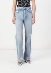Light blue flared jeans with a smooth texture, featuring five pockets, a zipper fly, and a classic denim design, paired with metallic shoes.