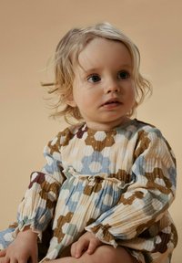 Puuvillamekko, jossa on kukallinen kuusikulmio kuvio sinisenä, ruskeana ja kermansävyisenä; mekossa on röyhelöhihansuut ja kerätty vyötärö. Kevyt, teksturoitu kangas.