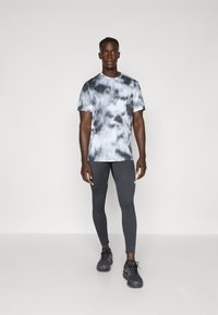 Short-sleeve, tie-dye t-shirt with gray and black patterns, paired with dark gray leggings. Model wears black athletic shoes.