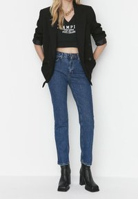 Blazer nero su una t-shirt grafica nera corta, abbinato a jeans blu a vita alta e stivali neri con tacco spesso.