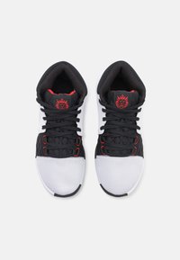 Scarpe sportive in bianco e nero con tomaia in rete testurizzata, linguetta imbottita, accenti rossi e cuciture intricate sui lati.