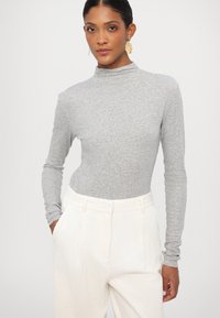 Gray long-sleeve turtleneck top made of soft fabric, paired with high-waisted, textured white pants. Features a fitted silhouette.