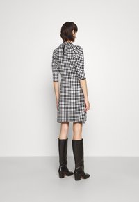 Robe en damier noir et blanc avec une silhouette ajustée, des manches trois-quarts, une fermeture éclair au dos et une longueur au genou, associée à des bottes noires jusqu'aux genoux.