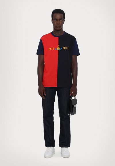 Color-blocked t-shirt featuring red and black sections, yellow text "1971" and "2071," plus a logo design. Paired with dark jeans and white sneakers.