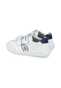 Zapatillas sintéticas blancas con tiras de Velcro, acentos en azul marino, punta redondeada, suela texturizada y un logotipo prominente en el costado.