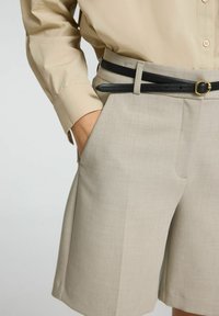 Beige shorts med skræddersyet pasform, udstyret med et sort læderbælte og guldspænde, med sidelommer og en glat tekstur.