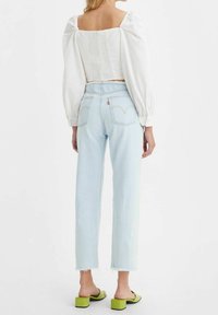 Vit topp med puffärmar och smockad baksida, ljusblå höga jeans och gröna klacksandaler. Avslappnad passform med fransade kantdetaljer.