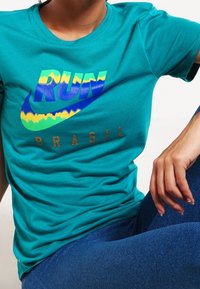Camiseta de algodón en color teal con un gráfico multicolor que dice "RUN" y el texto "BRASIL" en dorado. Mangas cortas y corte relajado.