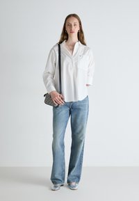Camicia bianca a maniche lunghe, jeans a campana azzurri chiari, scarpe argento e una borsa a tracolla con fantasia. Design semplice con una vestibilità comoda.