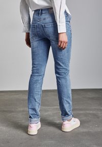 Vaaleansiniset farkut, joissa on istuva malli, takataskut ja keskipituinen vyötärö, yhdistettynä vaaleanpinkan värisiin lenkkareihin.