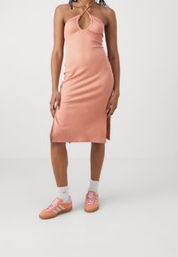 Robe à col halter côtelée en rose clair avec une fente sur le côté, associée à des baskets en suède roses et des chaussettes blanches mi-mollet. Texture lisse sur l'ensemble.