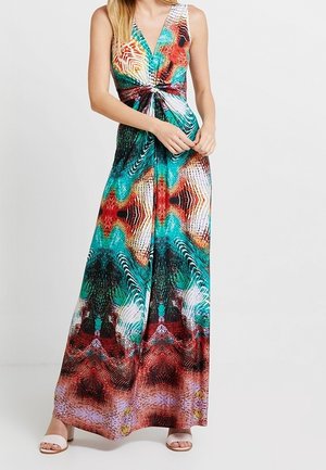 Mouwloze maxi-jurk met V-hals en een levendig multicolor abstract patroon, voorzien van een draaiknoopdetail in de taille, gedragen met witte open tenen hakken.