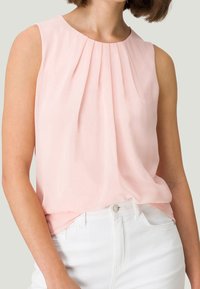 Blusa sin mangas de color rosa claro con pliegues en el escote, hecha de una tela suave y ligera, combinada con pantalones blancos de cintura alta.