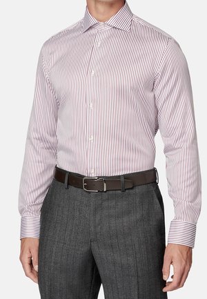 Homme portant une chemise blanche à fines rayures rouges verticales, ceinture marron foncé et pantalon gris à fines rayures, debout les bras détendus.