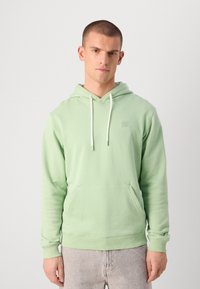 Sweat à capuche vert clair en matériau doux, avec une poche avant, des cordons blancs et un petit logo carré sur la poitrine.