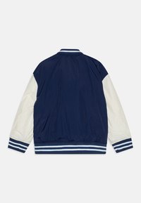 Veste bomber bleu marine avec manches blanches, poignets et ourlet côtelés rayés, et texture lisse. Comprend un col montant et une taille élastique.
