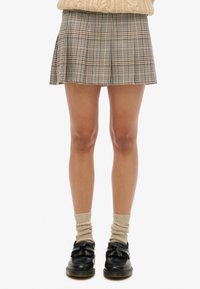 Geruite geplooide rok in beige, bruin en groene tinten. Afgewerkte zoom en lichte textuur, gecombineerd met zwarte schoenen en beige geribbelde sokken.