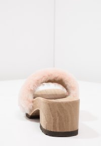 Chlupaté růžové bezpodpatkové dřeváky s dřevěnou podrážkou, vykazující zaoblený podpatek a hladký povrch, který ukazuje přirozenou dřevitou strukturu.