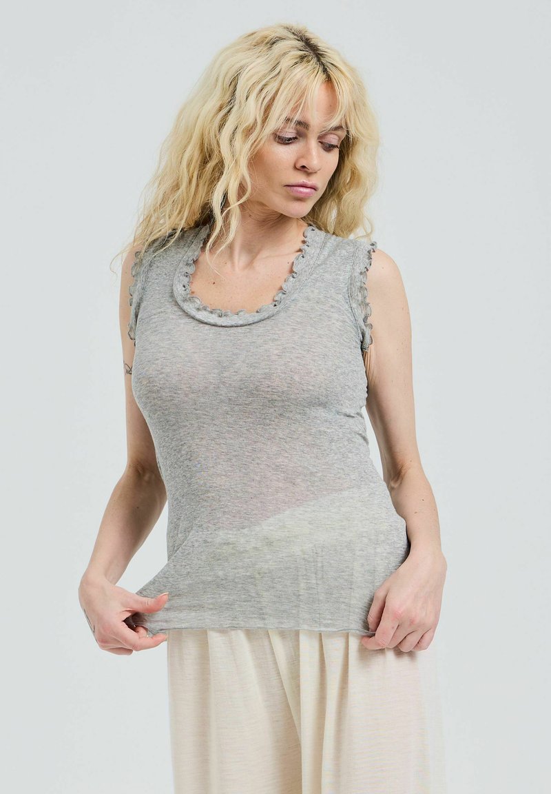 Haut à manches courtes, gris clair, avec un décolleté festonné et des bords volants, fabriqué en un matériau doux et transparent, porté sur une jupe crème fluide.