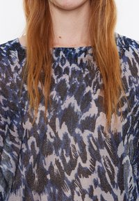 Transparante top met een blauw en zwart abstract patroon, met een losse pasvorm en een brede halslijn. Het materiaal heeft een lichte glans en een gestructureerde afwerking.