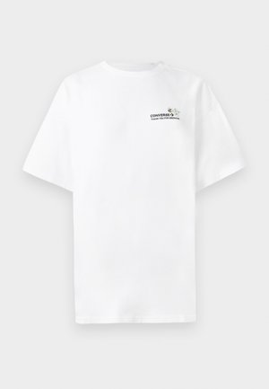 Valge lühikeste varrukatega T-särk, millel on väikene rinnatrükk, kus on kujutatud mesilast, lille ja tekst "CONVERSE, AITÄH, ET OLETE KASVANUD."