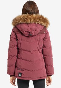 Chaqueta acolchada burdeos con capucha de piel sintética, textura acolchada, bolsillos laterales y parche de marca negro en el dobladillo. Cintura y capucha ajustables.