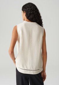 Ärmelloses Cremeoberteil aus leichtem Stoff mit geradem Schnitt und dekorativem perforiertem Saumdetail auf der Rückseite.