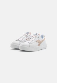 Zapatillas blancas con un acabado texturizado, que presentan un acento beige, una lengüeta rosa clara y una suela blanca gruesa con estrías verticales.