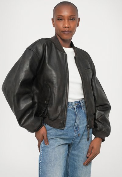 Must musta bomber-jakk, millel on lukuga es front, ribikaartega varrukad ja tasku detail. Koos helesiniste denim-ärkidega ja valge T-särgiga.