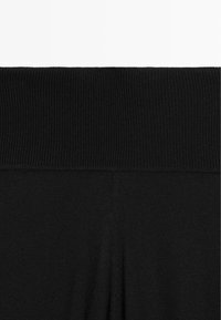 Schwarze Leggings mit einem breiten, gerippten Bund. Der Stoff wirkt weich und dehnbar, mit einer durchgehend glatten Textur.