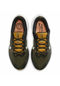 Pair of black and mustard Nike running shoes with white swoosh logos and smiley face design on the insoles, viewed from above.