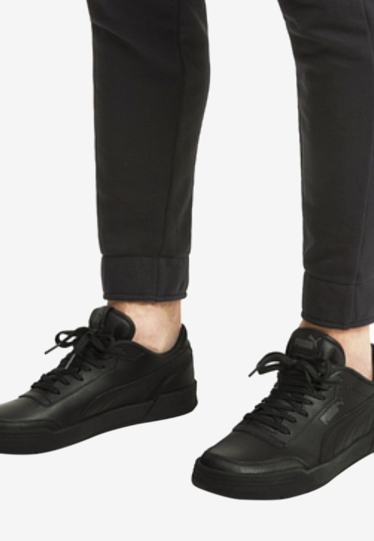 Baskets en cuir noir à profil bas, avec une tige texturée, des lacets ronds et une semelle en caoutchouc plate. Portées avec un pantalon foncé retroussé.