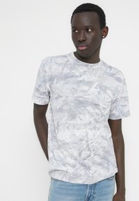 Γκρι μπλουζάκι με μοτίβο, στρογγυλή λαιμόκοψη και κοντά μανίκια, με διακριτικό αφηρημένο σχέδιο σε ανοιχτότερους τόνους του γκρι.