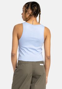 Ljusblå cropped tanktop med en tight passform och ribbad textur. Baksidan har breda axelremmar och en ren fåll, i kombination med olivgröna byxor.
