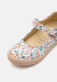 Blomstertrykt Mary Jane-sko med flerfargede blomster på hvit bakgrunn. Rund tå, beige teksturert gummisåle og justerbar reim.