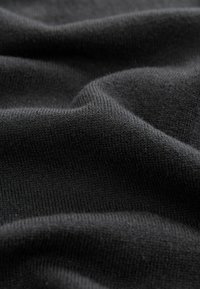 Zwarte gebreide stof met een zachte textuur, voorzien van een gladde, gelijkmatige weving en subtiele rek, gerangschikt in zachte golven.