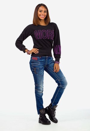 Schwarzer Sweatshirt mit "MORE" in Lila, kombiniert mit blauen Jeans mit Patchwork-Details und schwarzen Schnürkampfstiefeln mit Nieten.