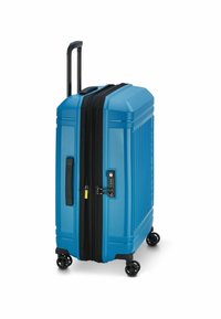 Maleta rígida azul con estrías verticales, cremallera negra y un candado de combinación. Cuenta con cuatro ruedas negras y un asa extensible.