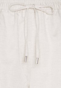 Close-up of beige fabric pants with an elastic waistband and tied drawstring featuring metal aglets at the ends.