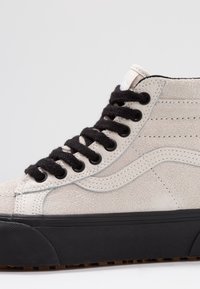 High-Top Sneaker aus hellgrauem Wildleder mit schwarzen strukturierten Schnürsenkeln, ausgestattet mit einer schwarzen Gummisohle und dezenten weißen Steppnähten.