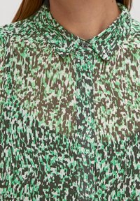 Camicia trasparente con colletto classico, chiusura con bottoni e un motivo astratto verde e marrone con una texture liscia.