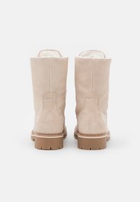 Botas de tobillo de ante beige con un forro interior suave, punta redonda y una suela de goma rugosa color tostado. Detalles de costura a lo largo de las costuras.