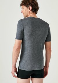 Grijze t-shirt met korte mouwen van zachte stof, met een ronde hals en een aansluitend ontwerp. Draag het met zwarte shorts, gezien van achteren.