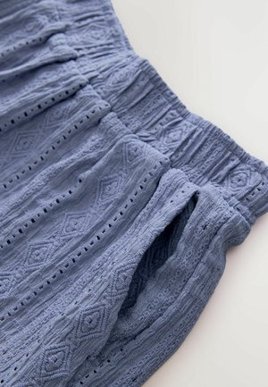 Tejido azul texturizado con un patrón de diamantes, que presenta una cintura elástica y bolsillos abiertos, destacando los intrincados detalles de tejido.