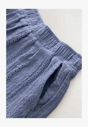 Zils teksturēts audums ar dimantu rakstu, ar elastīgu jostas atvērumu un vaļējām kabatām, izceļot smalkus aušanas detaļas.